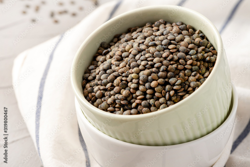 French green lentils in a bowl on the table, closeup. Dry unprepared green lentils. French green lentils in a bowl on the table, closeup. Dry unprepared green lentils.