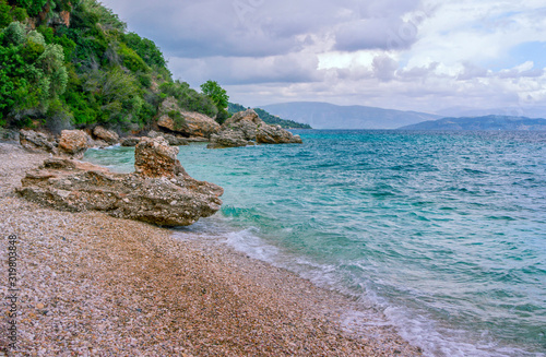 Beautiful summer landscape with sea  small village on the hill  bright colorful rainbow on blue sky  clouds and mountains on the horizon. Corfu Island  Greece