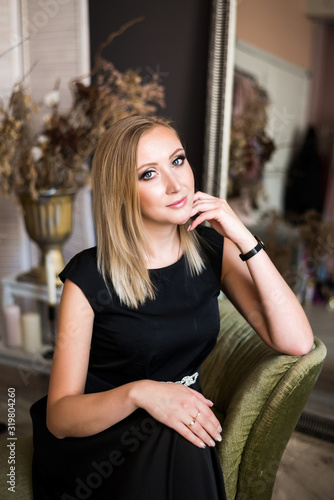 Portrait of a beautiful successful young blonde woman with professional makeup. Girl in a black dress posing sitting