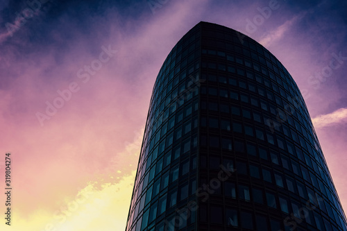 A tall modern business tower below a colorful sky