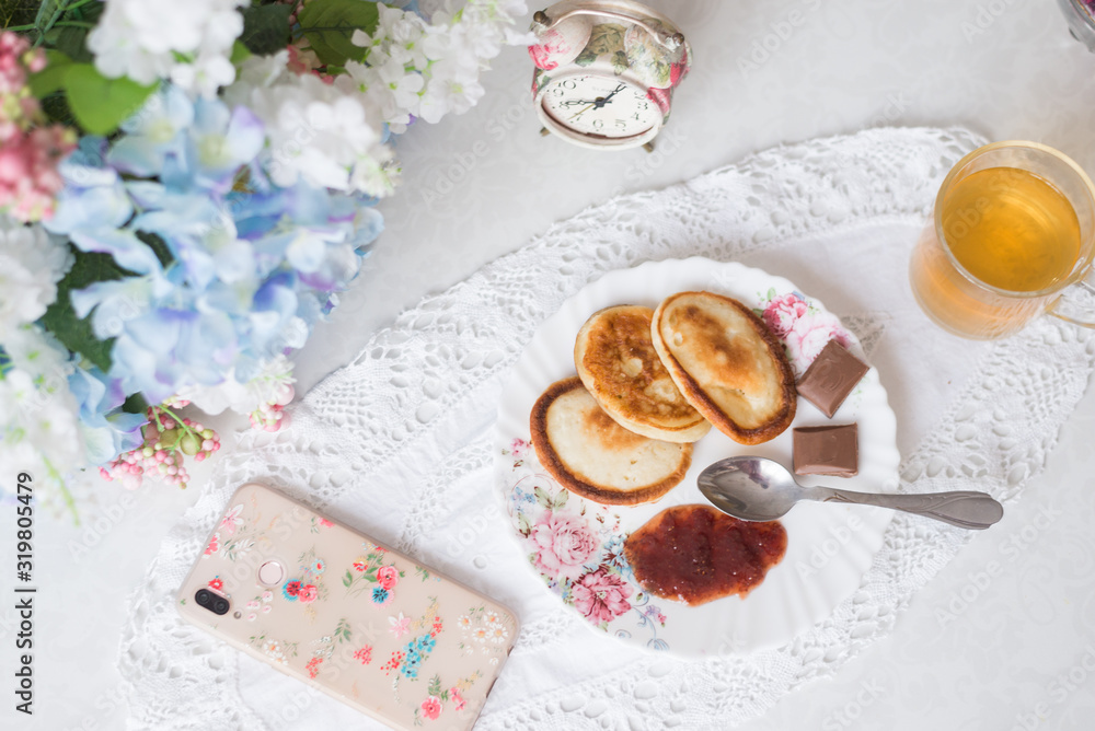 On the table with flowers pancakes with jam, green tea and sweets. Worth an alarm clock, the concept of Breakfast and sweet life On the table with flowers pancakes with jam, green tea and sweets. Worth an alarm clock, the concept of Breakfast and sweet life