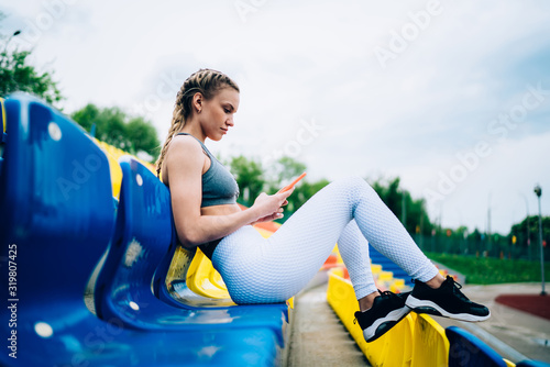 Sporty woman sitting and using smartphone at stadium