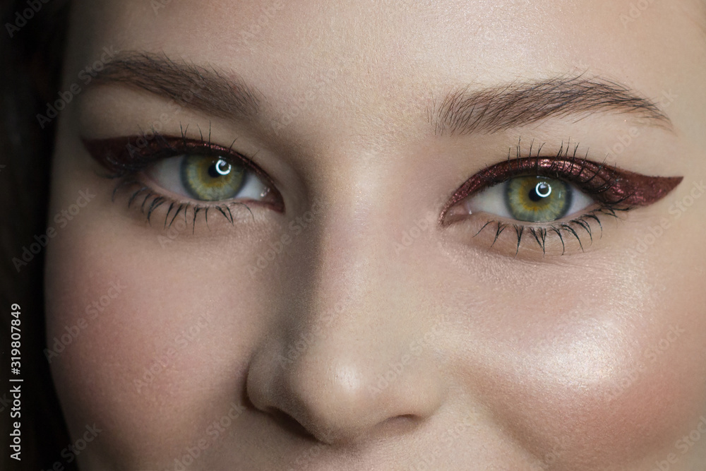 Fototapeta premium Beautiful woman with bright make up eye with sexy red liner makeup. Fashion big arrow shape on woman's eyelid. Chic evening make-up. Luxurious extremely long eyelashes. Shining face skin