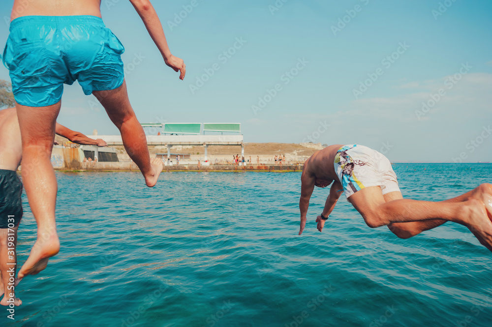 Group of happy crazy people having fun jumping in the sea water from boat. Friends jump in mid air on sunny day summer pool party at diving holiday. Travel vacation, friendship, youth holiday concept.