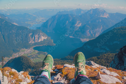 Legs of traveler in stylish green sneakers sitting on a high mountain cliff enjoying scenery mountain top. Pov view Hiking freedom concept. Austria Hallstatter See lake Krippenstein mountain Hallstatt © raisondtre