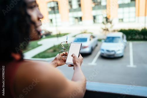 African American woman standing on balcony and using cellphone