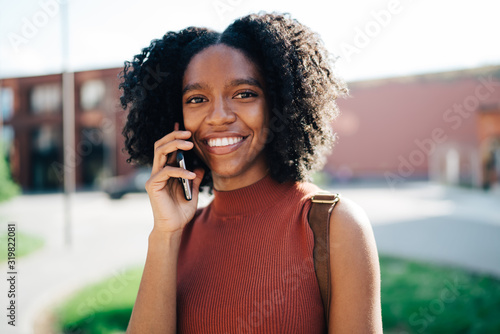 Young smiling black woman talking on smartphone at university