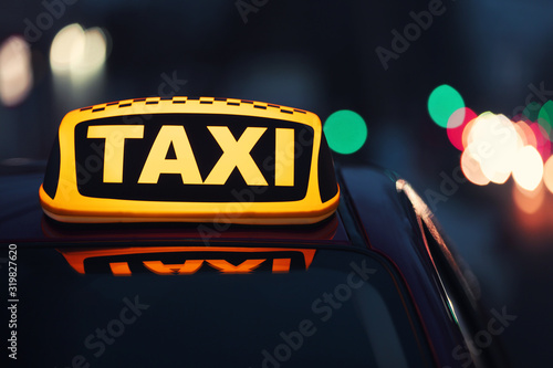 Taxi car with yellow roof sign on city street in evening, closeup