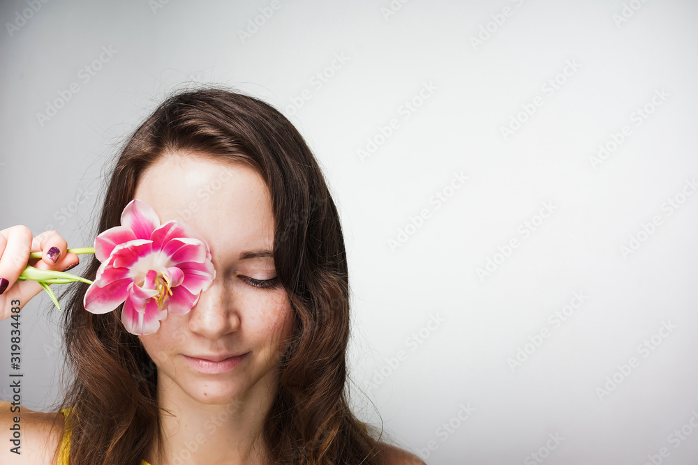a beautiful girl, covering her eyes, brought a tulip to her face. gray background