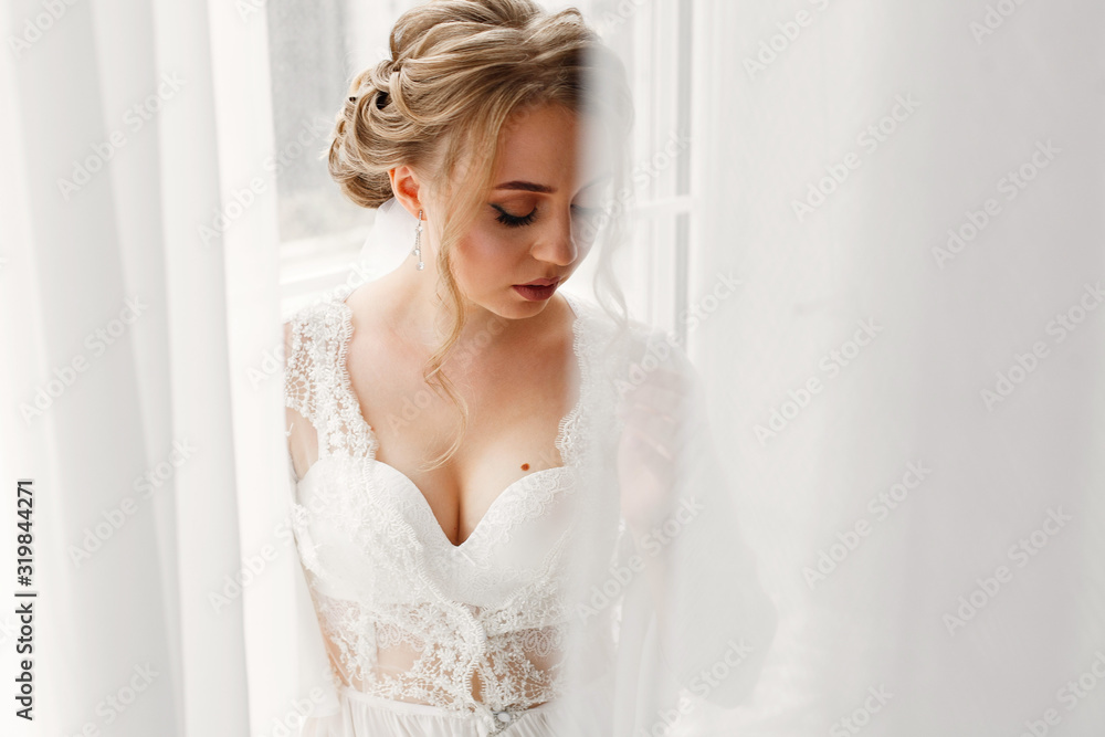 portrait a sexy blonde woman in underwear near big window . morning of  beautiful bride in hotel room with stylish white interior. young womans face with attractive neckline in white  dress close up.