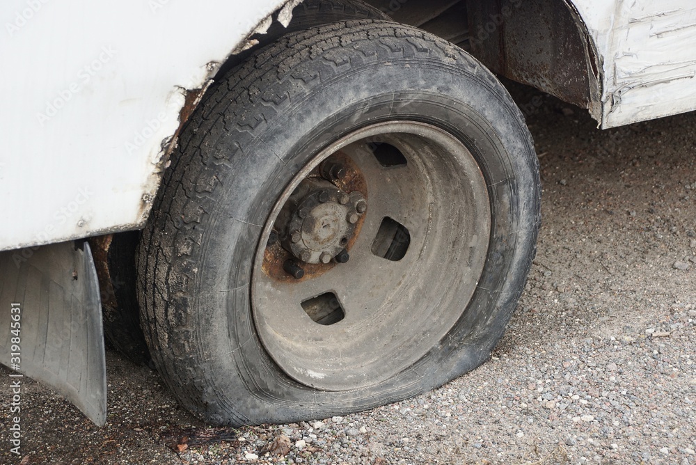 one black flat tire on a white car on gray asphalt in the street one black flat tire on a white car on gray asphalt in the street