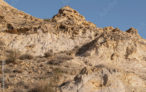 a steep rocky hillside in the judean desert mountains above near ein mabo'a in the west bank showing exposed layers of limestone, chalk, flint and sparse vegetation