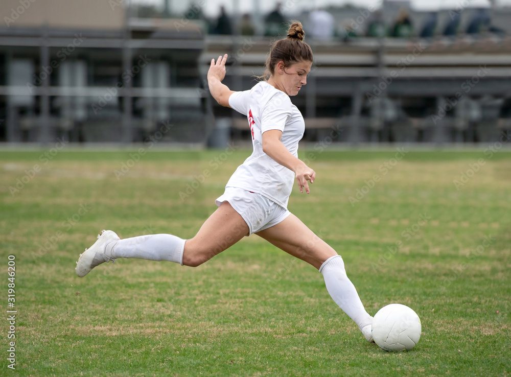 Young girl playing in a soccer game and kicking the ball