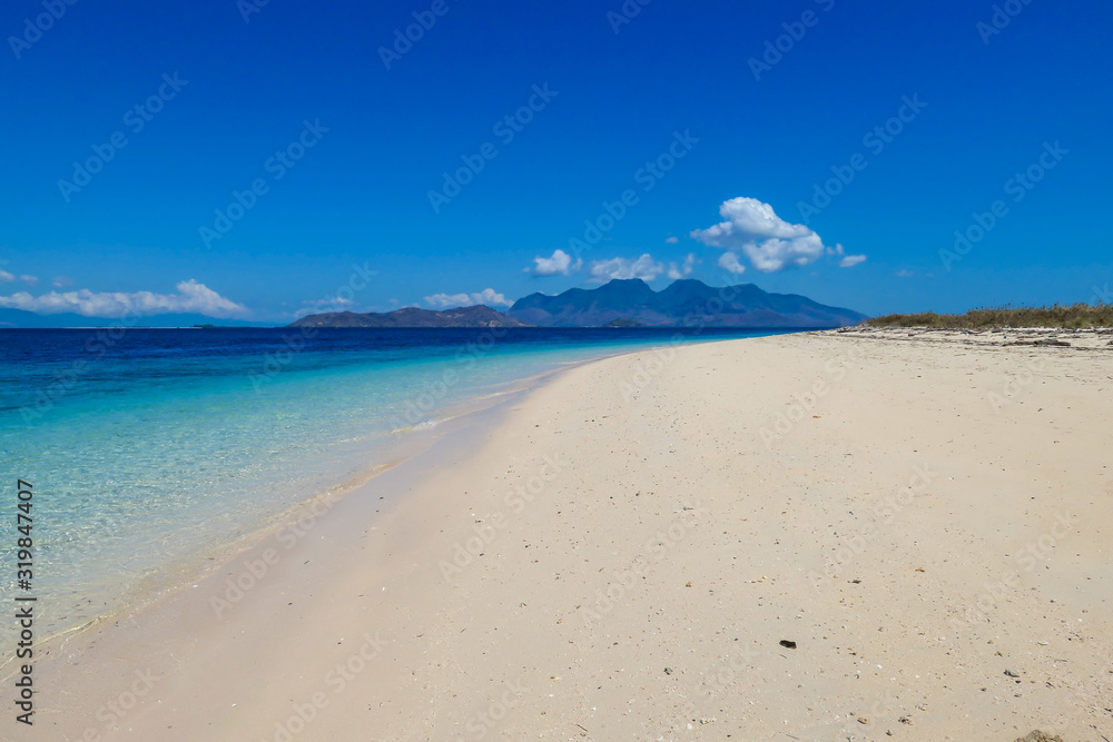 A view on white sand beach on a small island near Maumere, Indonesia. Happy and careless moments. Waves gently washing the shore. Clear, turquoise coloured water displaying coral reef. Hidden gem.
