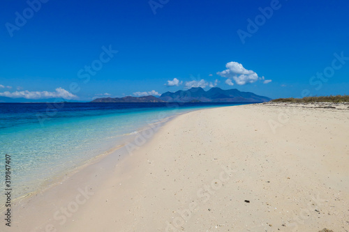 A view on white sand beach on a small island near Maumere  Indonesia. Happy and careless moments. Waves gently washing the shore. Clear  turquoise coloured water displaying coral reef. Hidden gem.