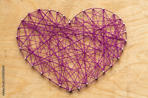 The heart is made of purple threads wrapped on nails embedded in a wooden board. View from above