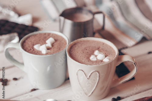 Two cups of hot cocoa with marshmallows and cinnamon sticks on wooden background. Love. Cocoa drink. Valentines day treat ideas.