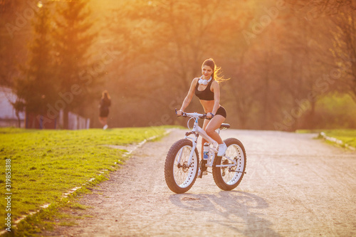 young girl with a beautiful figure riding a bike on the road at sunset in the park
