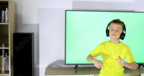 Little boy dancing. Child with headphones dancing and singing in front of television.
