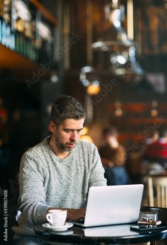 Middle-aged man working on a laptop computer, sitting at the cafeteria, lifestyle concept