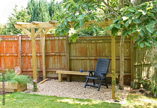 OTTERY ST MARY, DEVON, ENGLAND - 25TH JULY 2019: A lounger chair is positioned in the shade of a pergola and a magnolia tree in an English country garden.