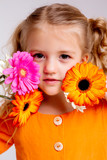 little blonde girl in an orange dress holds tulips and gerberas in her hands on a white background, a child girl smiles and holds spring flowers in her hands, space for text
