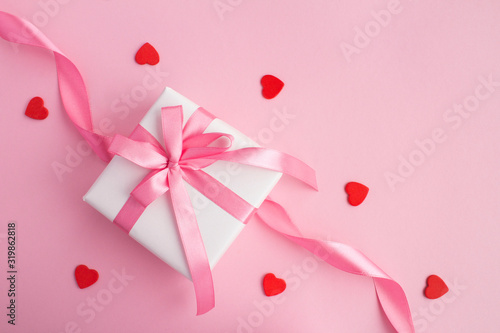 Gift with pink  bow  and red  hearts on the pink background. Top view. Copy space.