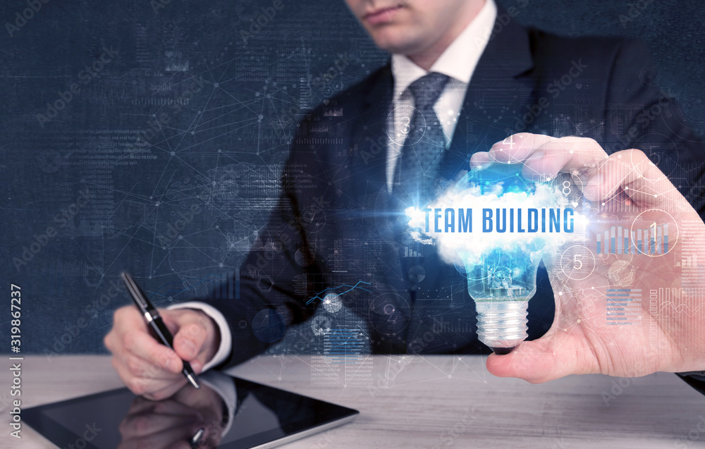 Businessman holding a light bulb with TEAM BUILDING inscription, new business concept Businessman holding a light bulb with TEAM BUILDING inscription, new business concept