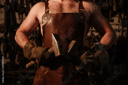 Brutal artisan blacksmith standing in a workshop with two hammers close up