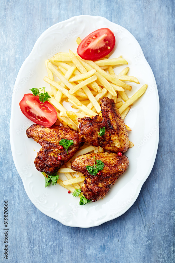 Spicy chicken wings with french fries and tomatoes. Bright wooden background. Top view. Spicy chicken wings with french fries and tomatoes. Bright wooden background. Top view.
