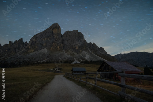 Night shot full of stars of trail in countryside with huts and startrail sass de putia in background during autumn