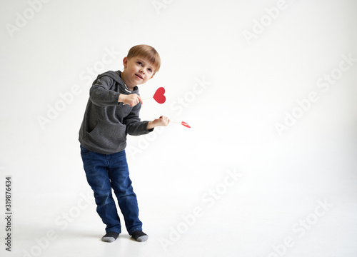 Sweet boy playing with two red paper hearts on sticks. Valentines day or kids healthcare, medical concept