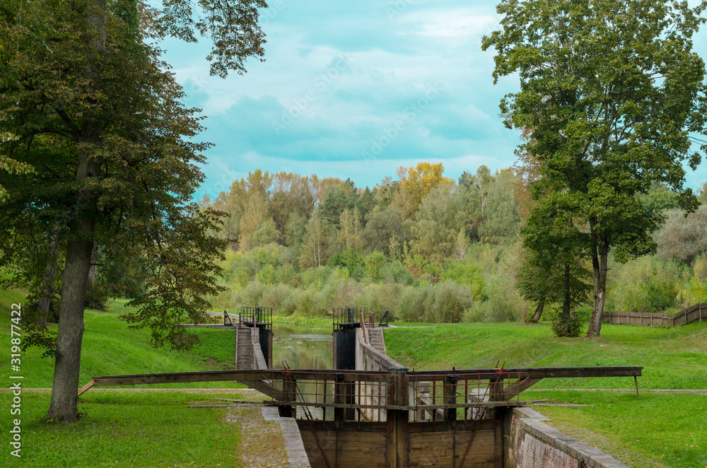 Fototapeta premium Old gateway on the channel. Wooden dam on the river. Autumn landscape.