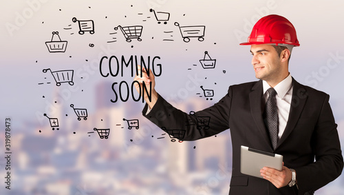 Handsome businessman with helmet drawing COMING SOON inscription, contruction sale concept