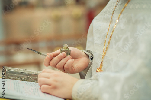 Foto priest holds in his hands a bottle with miro and a brush for making anointing on