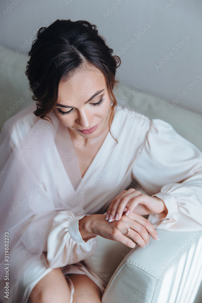 Morning bride, beautiful bride is waiting for the wedding sitting on the sofa in the white room. Girl in wedding dress posing on the sofa Morning bride, beautiful bride is waiting for the wedding sitting on the sofa in the white room. Girl in wedding dress posing on the sofa