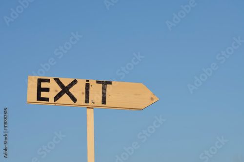 Wooden arrow sign with the word exit. In the background the blue sky