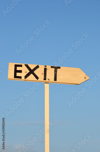 Wooden arrow sign with the word exit. In the background the blue sky