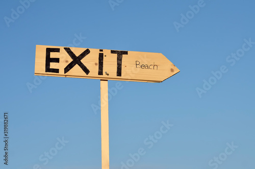 Wooden arrow sign with the word exit beach. In the background the blue sky