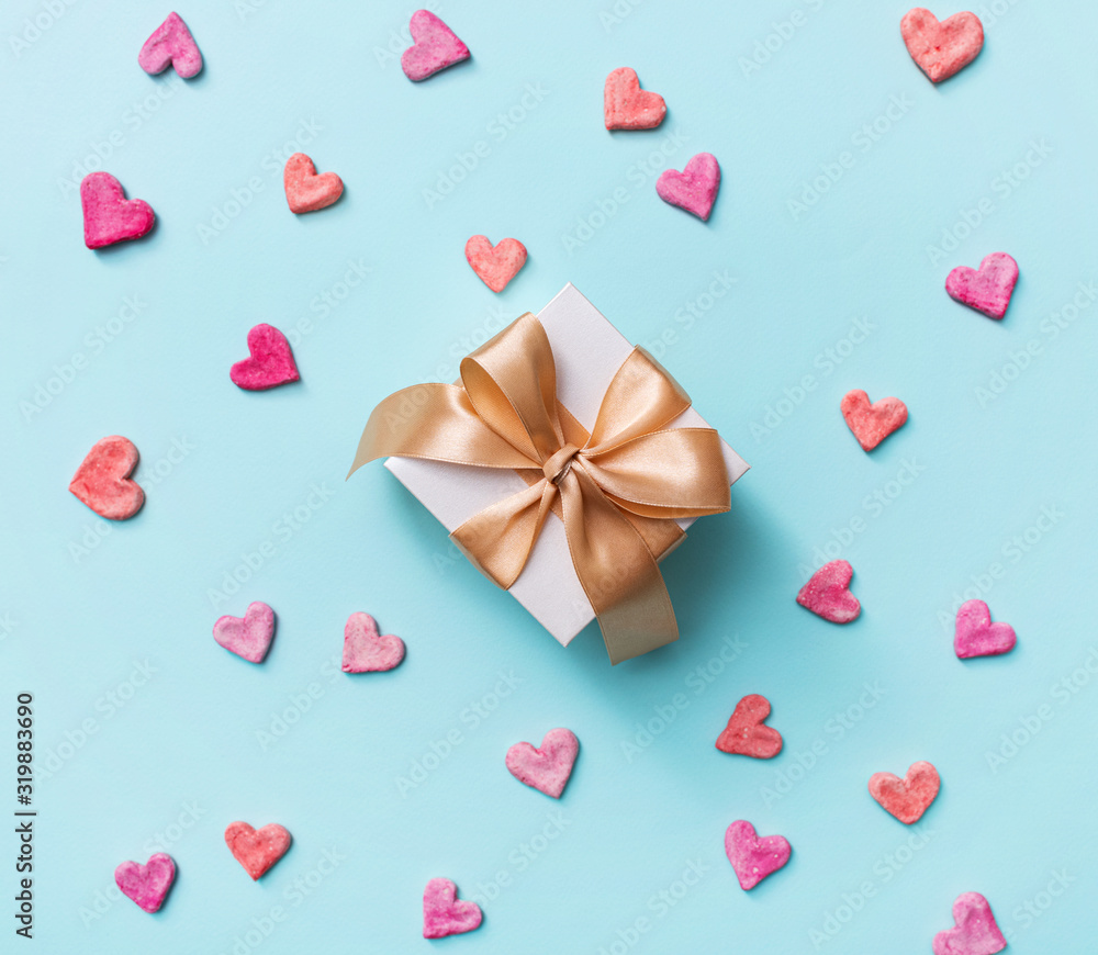 Close up of gift box with golden tied bow, among heart shapes. Top view holiday background.