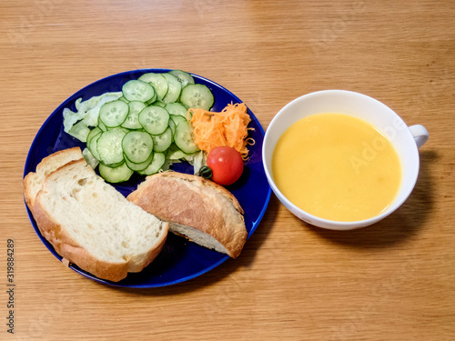 木のテーブルの上に置いてある自家製パンとサラダと温かいカボチャスープの朝食メニュー