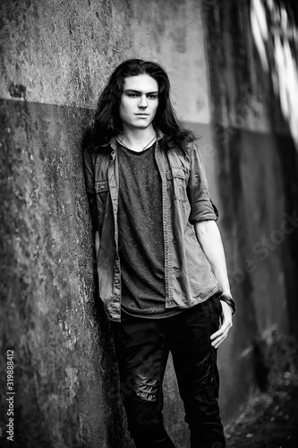 a black-and-white photo of a young man with long, dark hair and brown eyes, a face with freckles, walking down the street in a stylish shirt and jeans,in a Cagle style, in a sad mood photo
