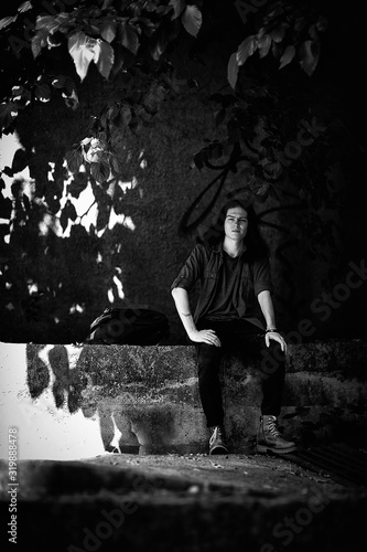 a black-and-white photo of a young man with long  dark hair and brown eyes  a face with freckles  walking down the street in a stylish shirt and jeans in a Cagle style  in a sad mood