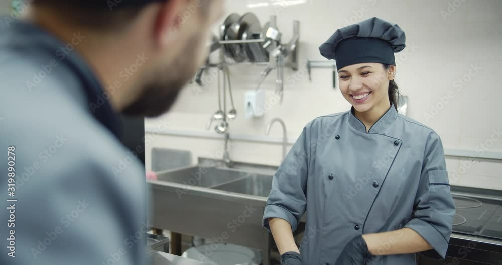Professional female chef in working clothes, hat and rubber gloves cooking in restaurant kitchen with her male partner. Concept of teamwork and support Professional female chef in working clothes, hat and rubber gloves cooking in restaurant kitchen with her male partner. Concept of teamwork and support