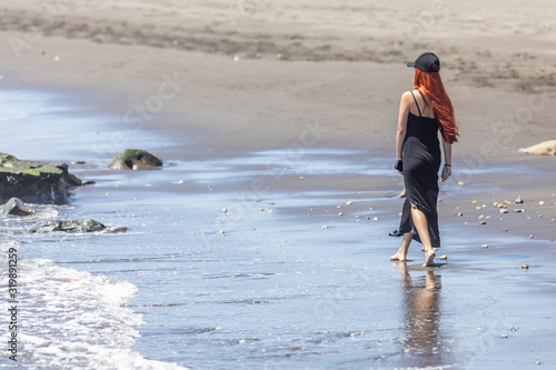 Young girl with a black dress and hut walking at the wet coast in a beach inside an awe natural scenery at Chilean coast. Enjoying vacations with a relaxing walk inside a tranquil beach scene 