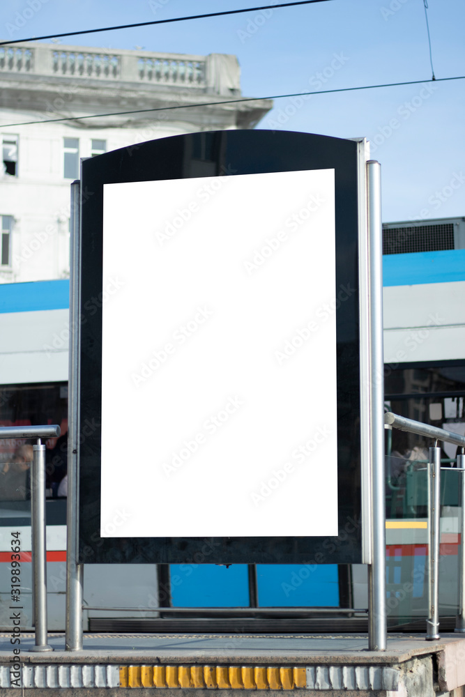 Advertising sign at the tram station stop. The tram passes in the background. Advertising sign at the tram station stop. The tram passes in the background.