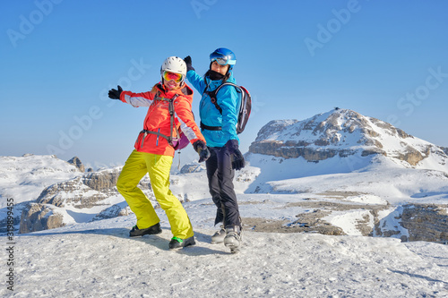 Two women skiers posing at Sass Pordoi (Pordoi peak), with Piz Boe mountain peak in the background, during a break from the Sellaronda ski tour, on a bright Winter day.