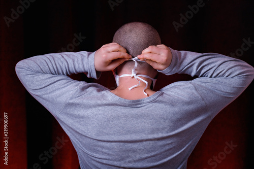 A man standing back to camera tying a medical gauze mask on dark red background. Virus preventive methods. Protection of upper and lower respiratory system from  Chinese coronavirus concept.
