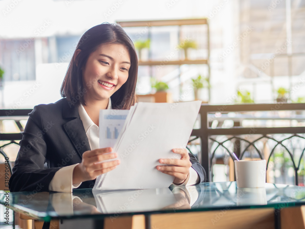 Happy Asian business woman sitting and looking document in cafeteria. Adorable Asian business woman smiling while success in job at cafeteria.