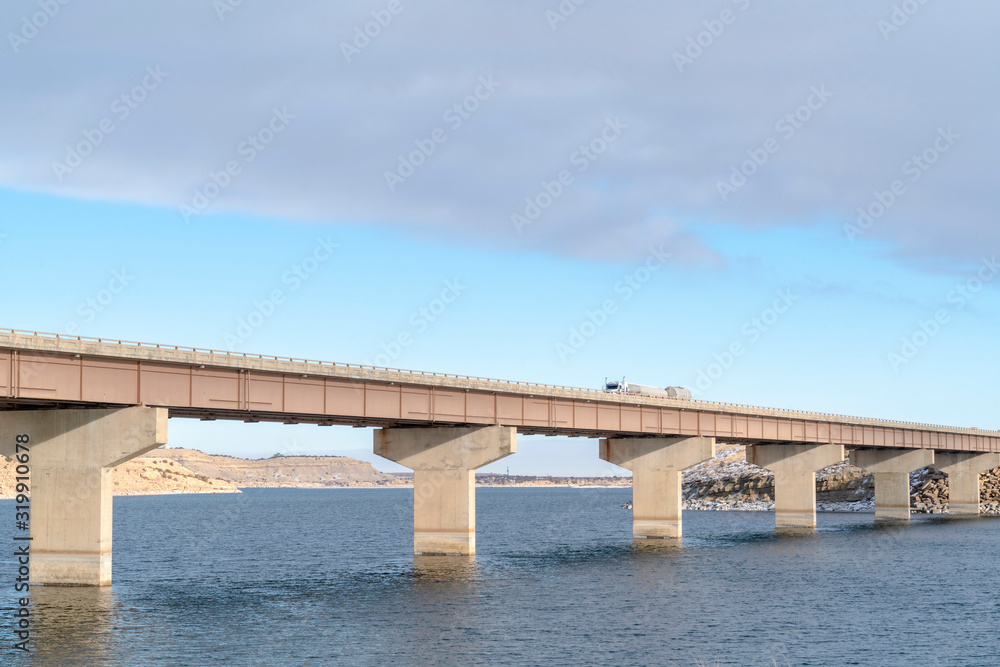 Stringer bridge supported by abutments ovelooking lake land and cloudy sky